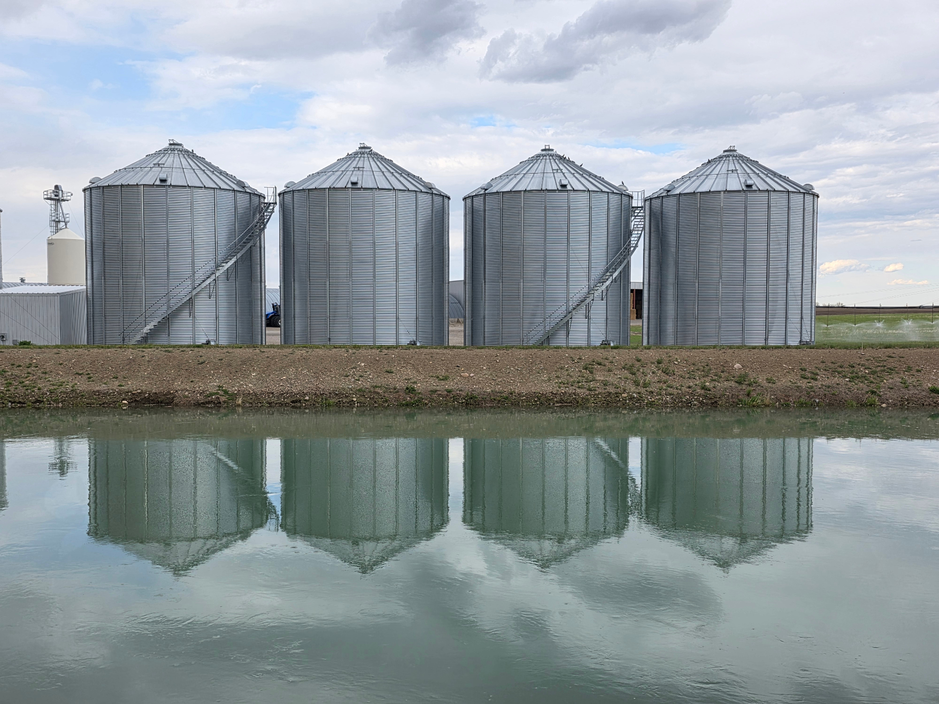 Row of grain bins reflected in still water on the Prairies